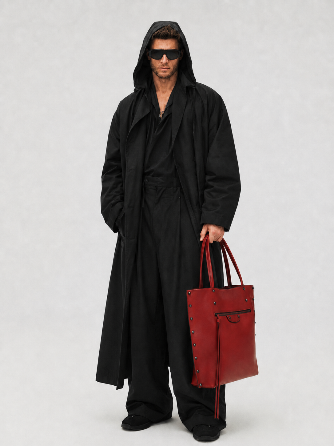 Model in an all-black hooded look carrying a red bag