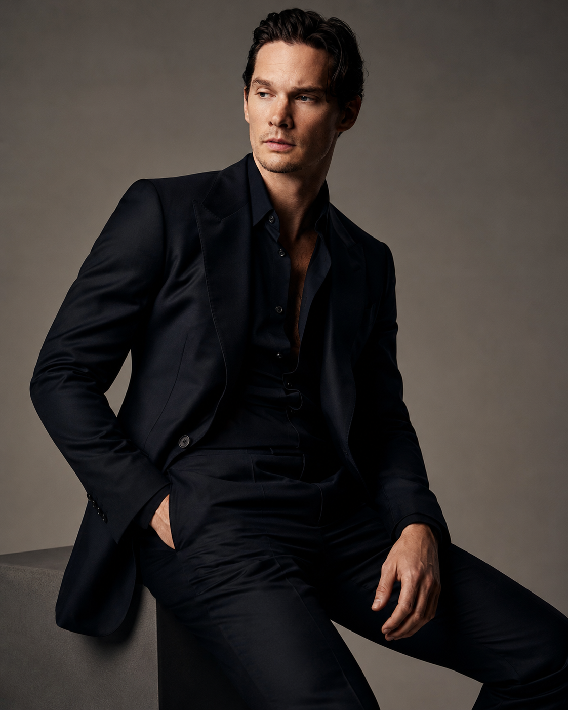 Model in a dark tailored look seated against warm grey